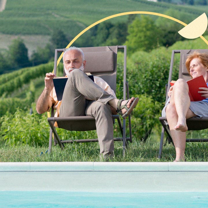 An older white couple sits together outside while reading books.