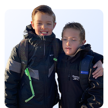 An image of two young boys wearing rain coats and backpacks.